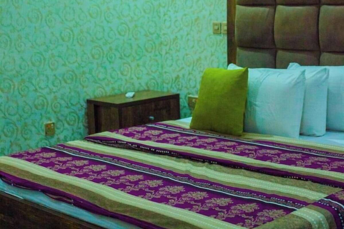 A bedroom with a patterned wallpaper, a bed with a headboard, a nightstand, and an air conditioning unit.