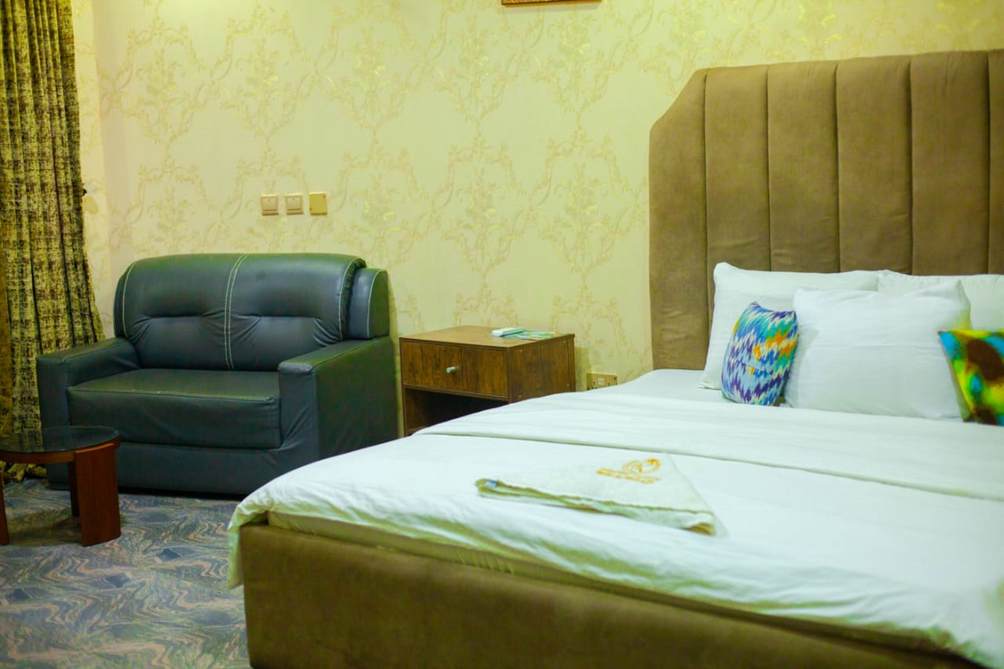A hotel room with a large bed, a leather armchair, a wooden nightstand, and a small table.