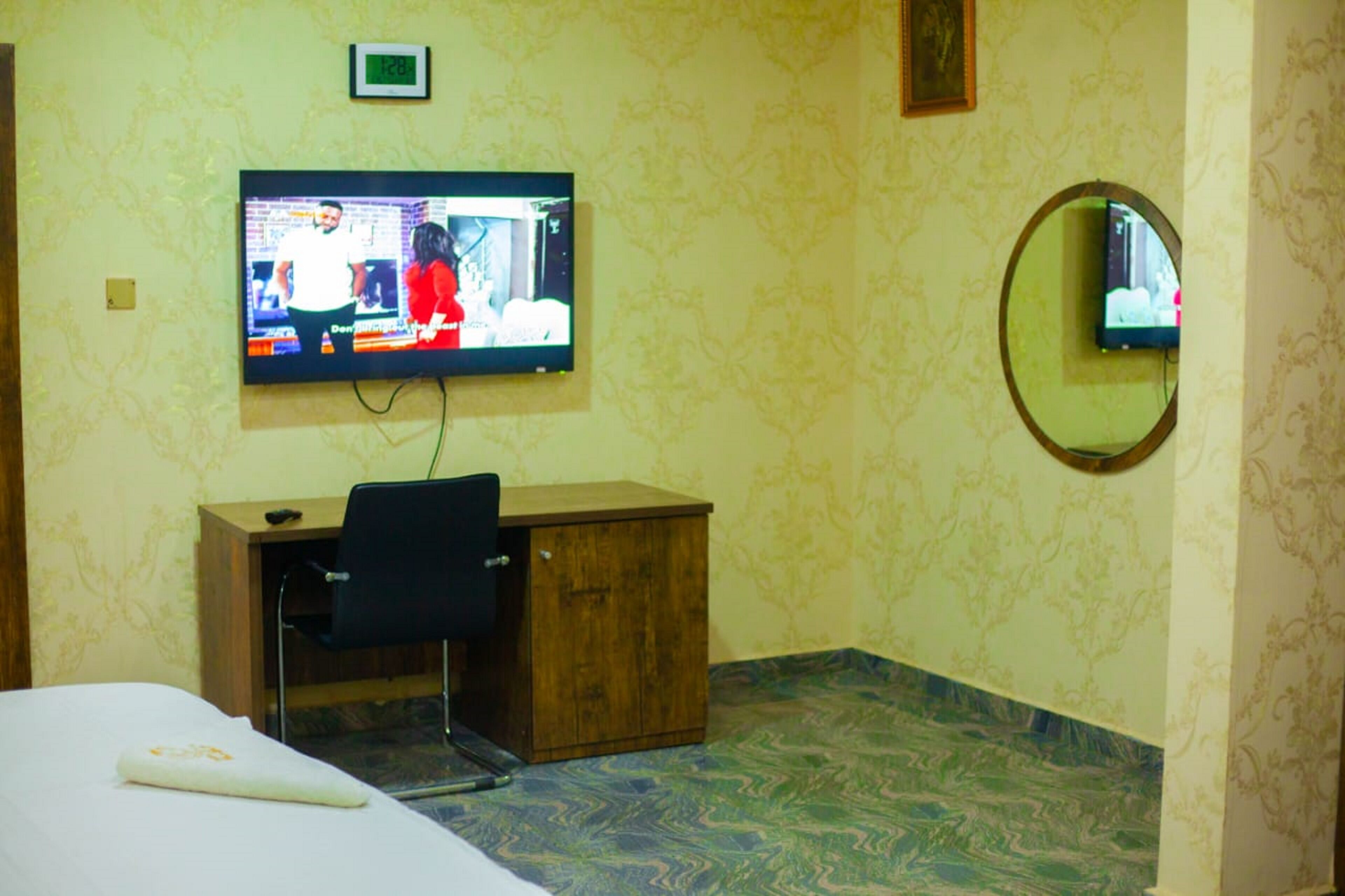 A hotel room with a bed, a desk, a chair, a television on the wall, and a mirror.