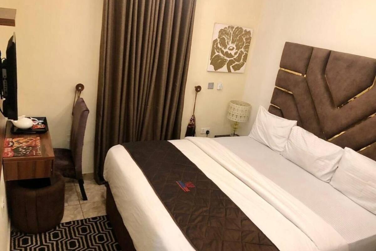 A hotel room with a bed, a desk, a lamp, and a curtain.