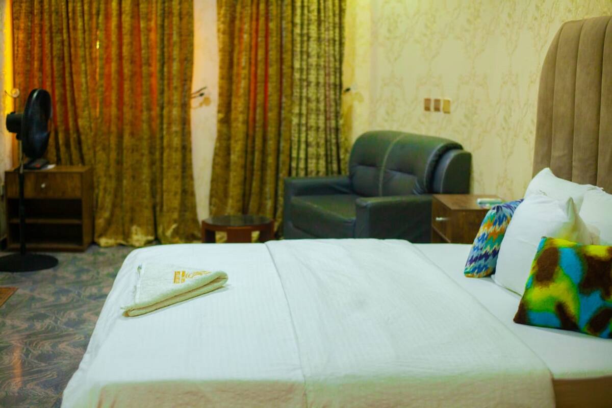 A hotel room with a bed, a chair, a small table, and curtains.