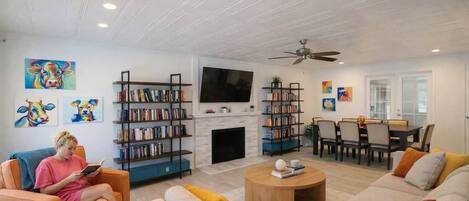 A living room with a fireplace, bookshelves, a TV, and a dining area.