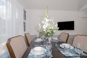 Mesa de comedor preparada para cuatro personas, con un florero, copas de cristal y platos.