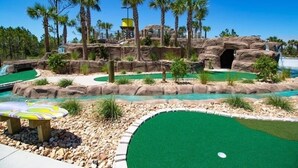 Un parcours de minigolf agrémenté de formations rocheuses, de palmiers et d’un petit élément décoratif aquatique.