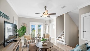 Un vaste salon doté d’un téléviseur à écran plat, d’un ventilateur de plafond, d’une table basse et d’un escalier menant à un autre niveau.