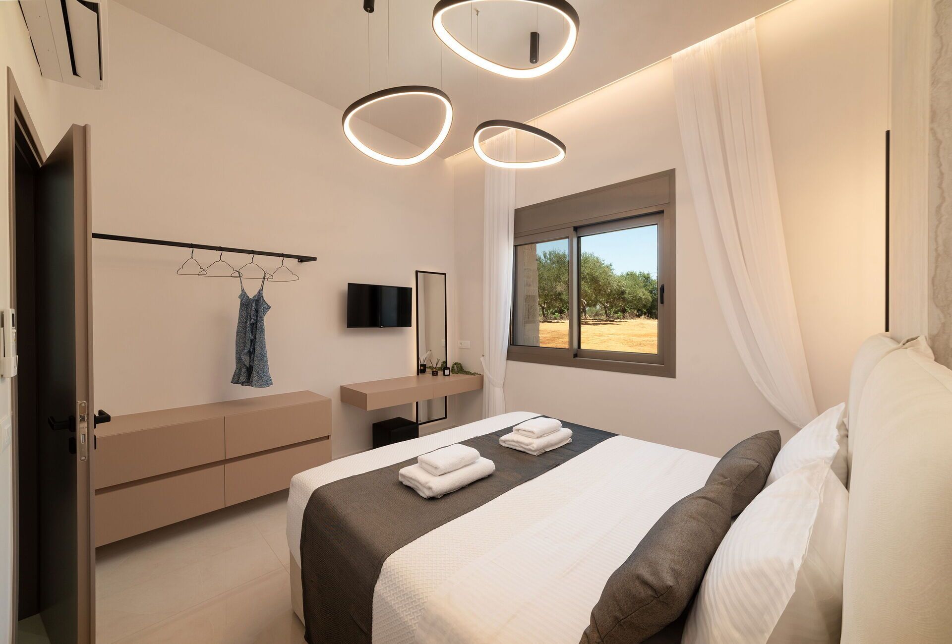 A modern bedroom with a bed, bedside tables, a TV, and a window with a view of trees.