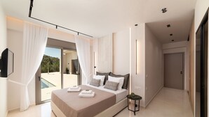 A modern bedroom with a large bed, a small side table, and a view of a pool and greenery. - Villa El - Luxury villa for an exclusive vacation in Crete (Kournás)