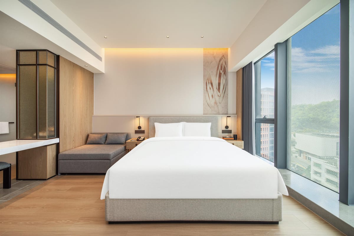 Une chambre d’hôtel moderne dotée d’un grand lit, d’un coin salon, d’un bureau et d’une grande fenêtre donnant sur la ville.
