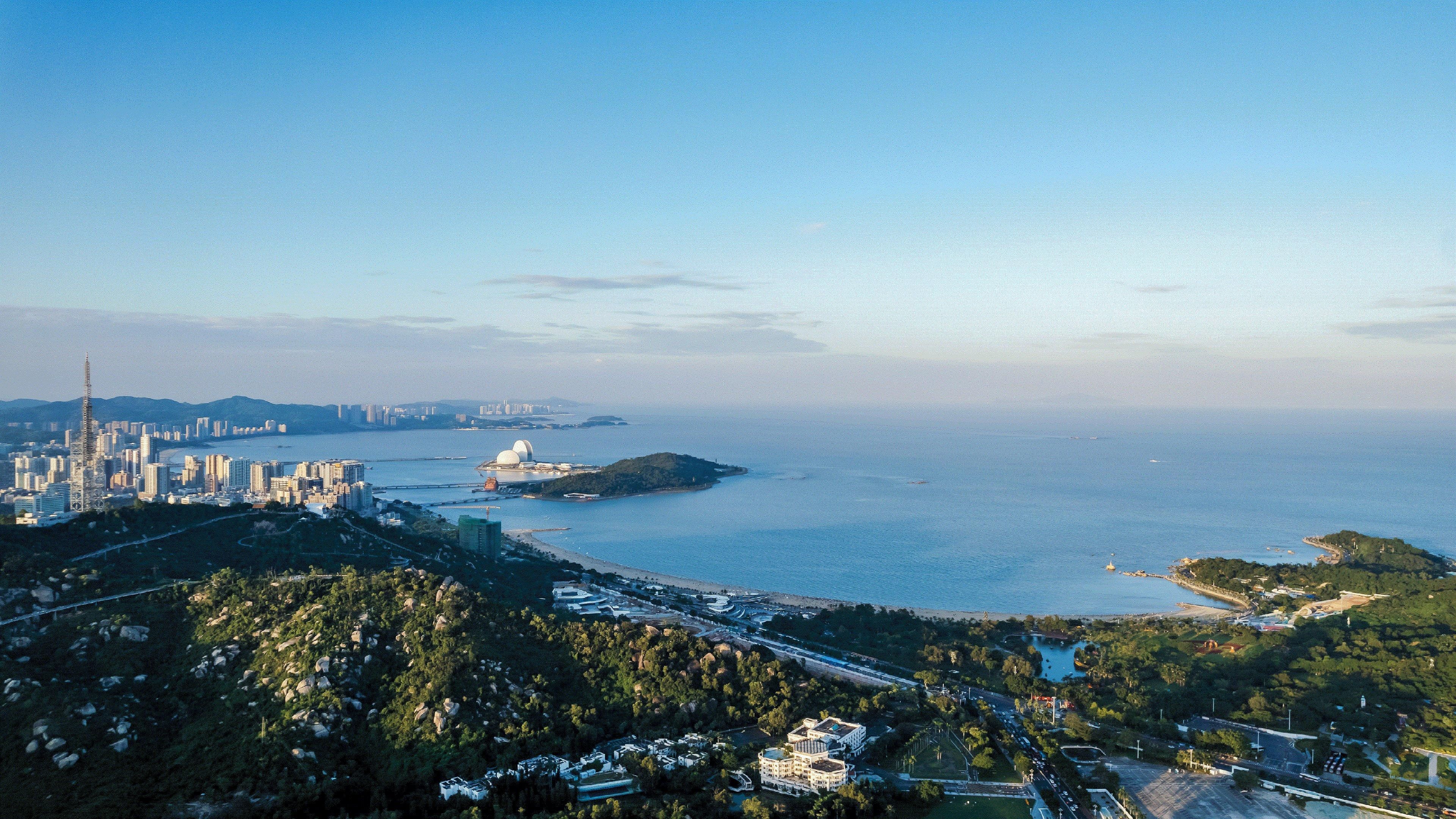 A coastal cityscape with a prominent tower, dense urban area, and a large body of water.