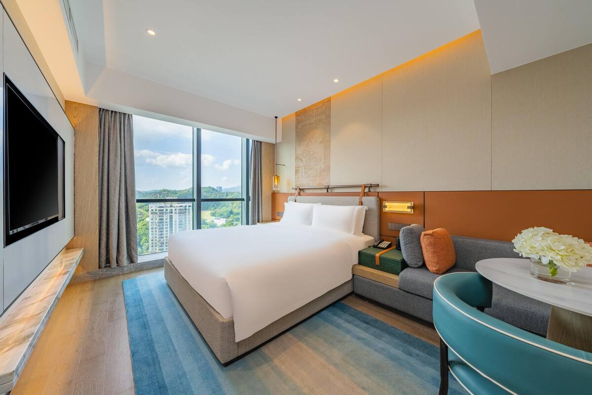 Une chambre d’hôtel moderne avec un grand lit, un canapé, une petite table agrémentée de fleurs et un téléviseur.