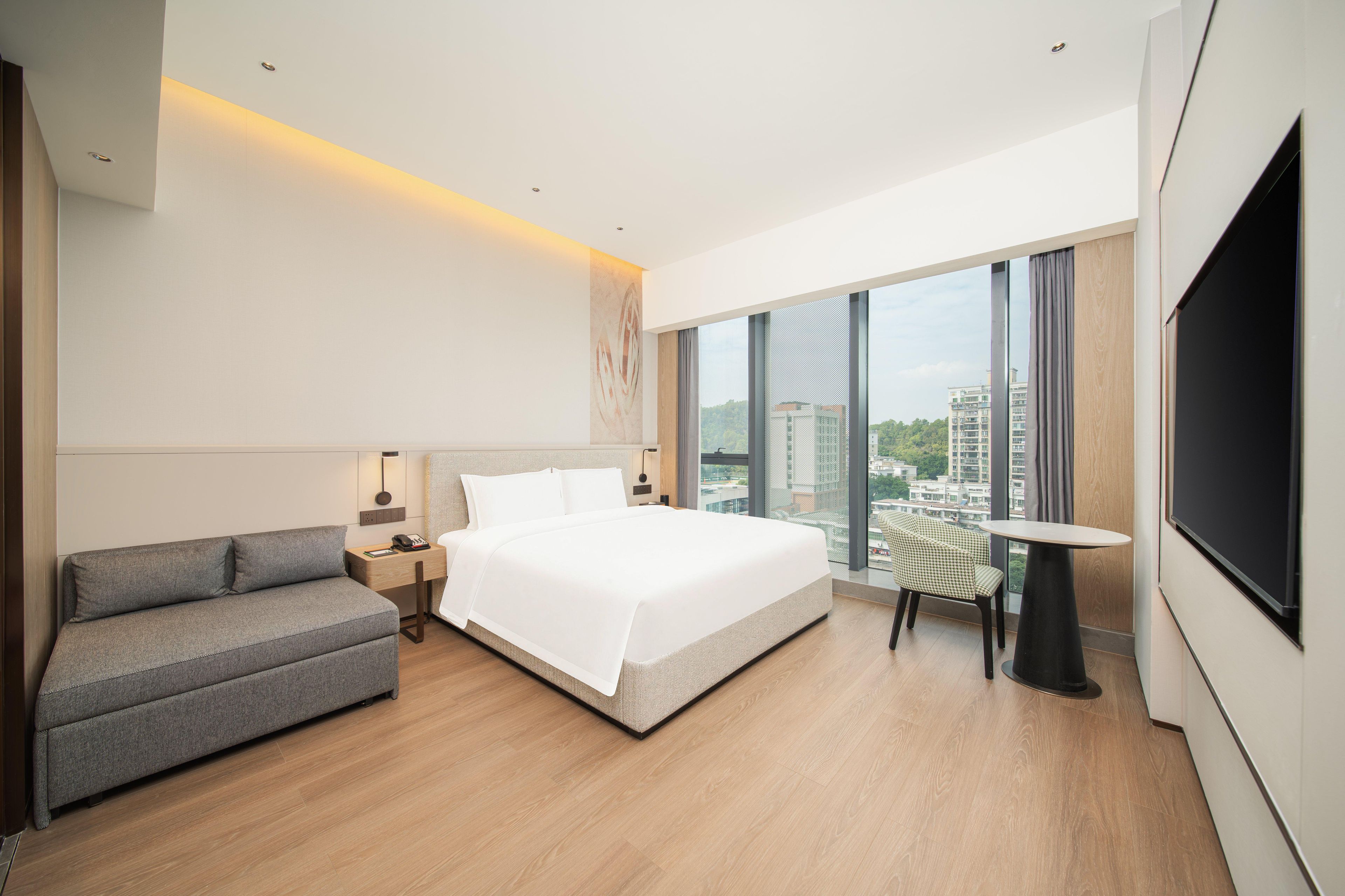 Una habitación de hotel moderna con una cama grande, un sofá, una mesita y un televisor.