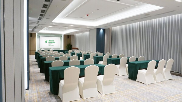 A conference room with rows of tables and chairs, a projector screen, and a presentation area. - Holiday Inn Zhuhai City Center (Zhuhai)