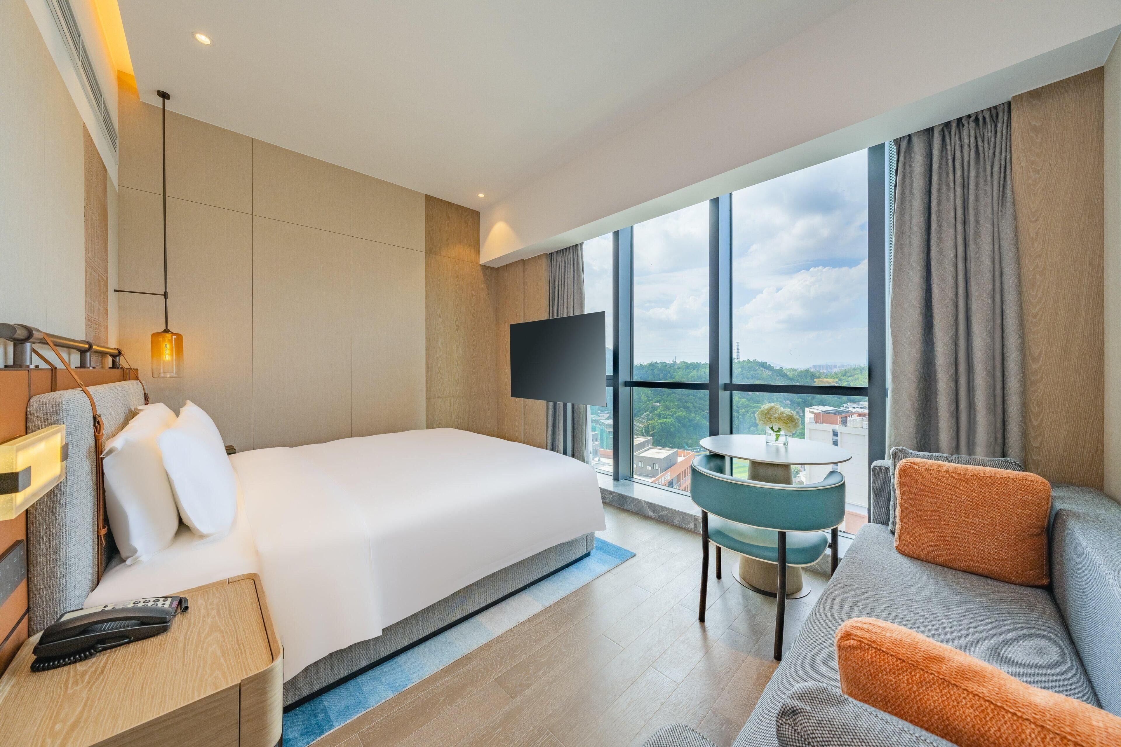 Een hotelkamer met een bed, een televisie, een bank, een tafeltje en uitzicht op de stad.