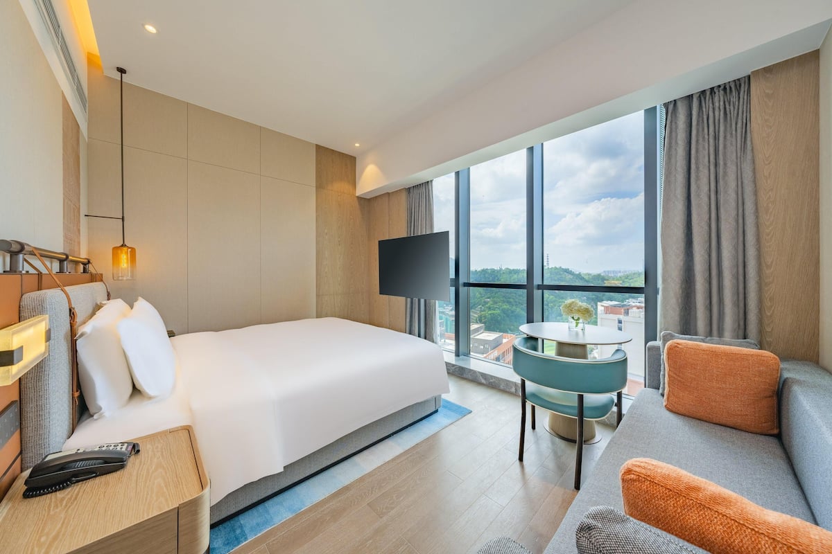 Une chambre d’hôtel avec un lit, une télévision, un canapé, une petite table et une vue sur la ville.