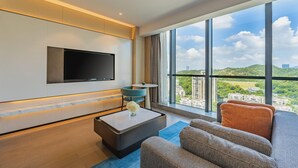 A modern hotel room with a large window, a flat-screen TV, a sofa, a coffee table, and a small table with a vase. - Holiday Inn Zhuhai City Center (Zhuhai)