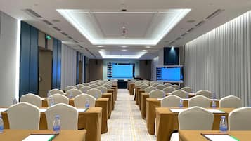 A conference room with rows of tables, chairs, and a large screen at the front.