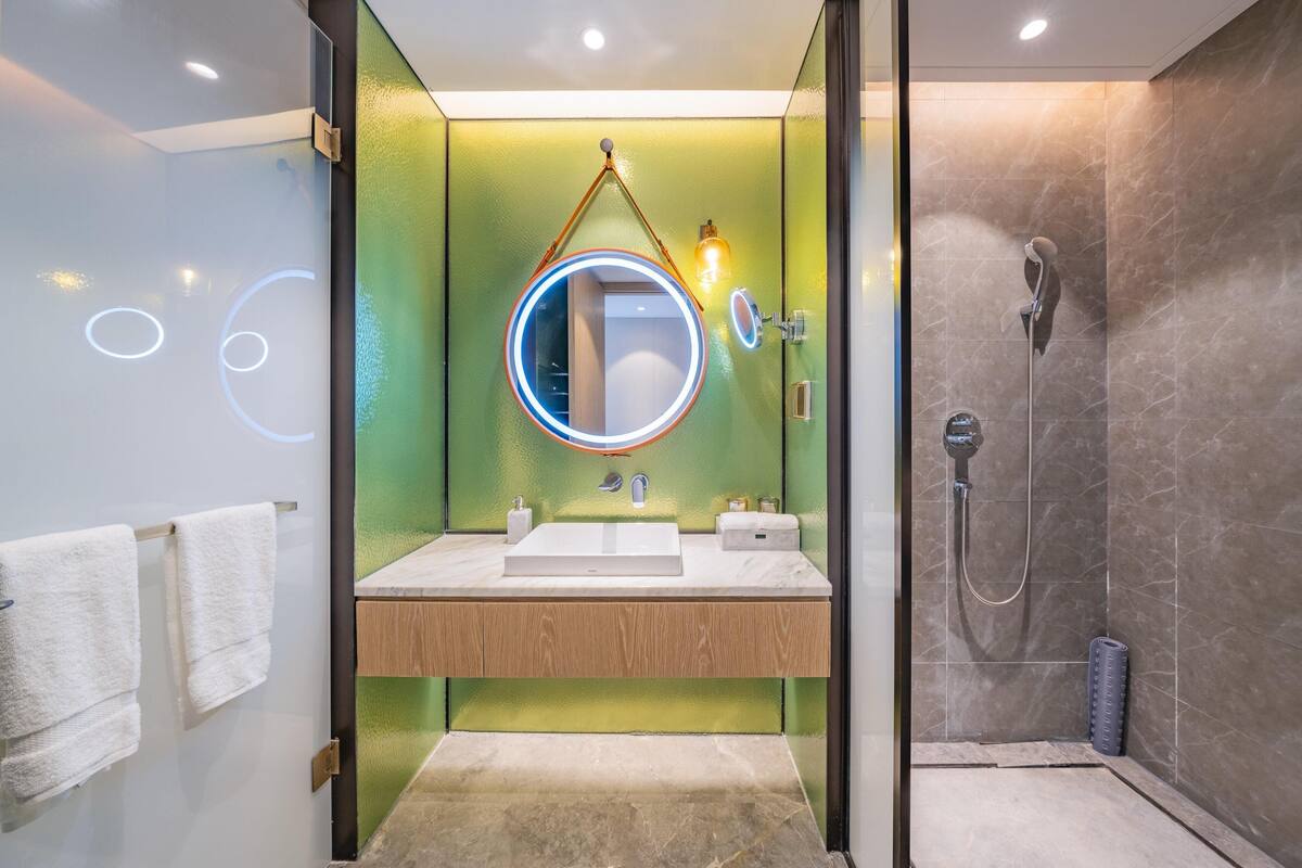 Une salle de bain moderne avec une douche à parois de verre, un meuble-lavabo en bois et un grand miroir rond doté de lumières intégrées.
