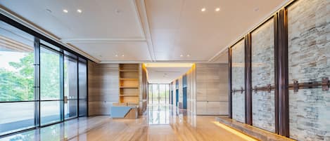 A modern hotel lobby with a wooden floor, glass doors, a reception desk, and a cityscape view.