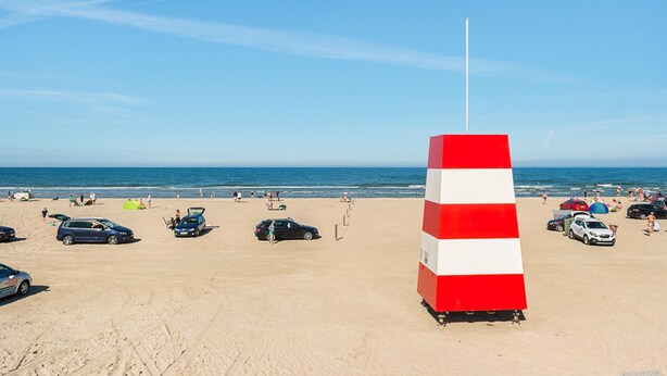 A beach with a red and white striped pole, cars parked, and people in the background. - First Camp Lakolk strand- Römö (Rømø)