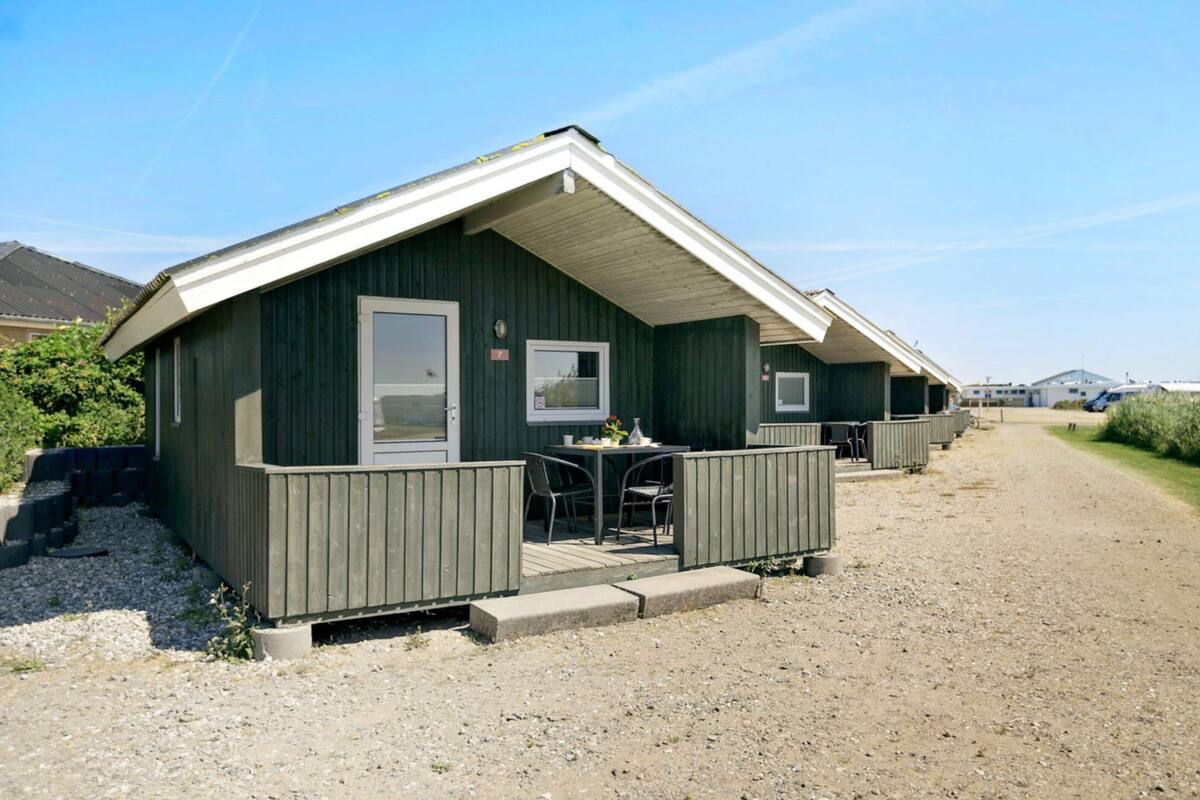 A row of small, single-story cabins with a gravel driveway and a clear sky.