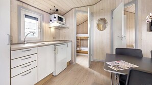 A compact kitchen with white cabinetry, a microwave, and a sink. There is a dining area with a table and chairs, and a small round mirror on the wall. - First Camp Lakolk strand- Römö (Rømø)