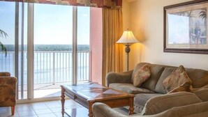 A living room with a sofa, a coffee table, and a lamp. There is a large window with a view of the sea.