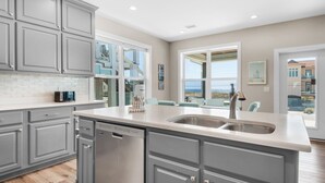 Una cocina moderna con armarios grises, lavavajillas y un amplio ventanal con vistas al mar.