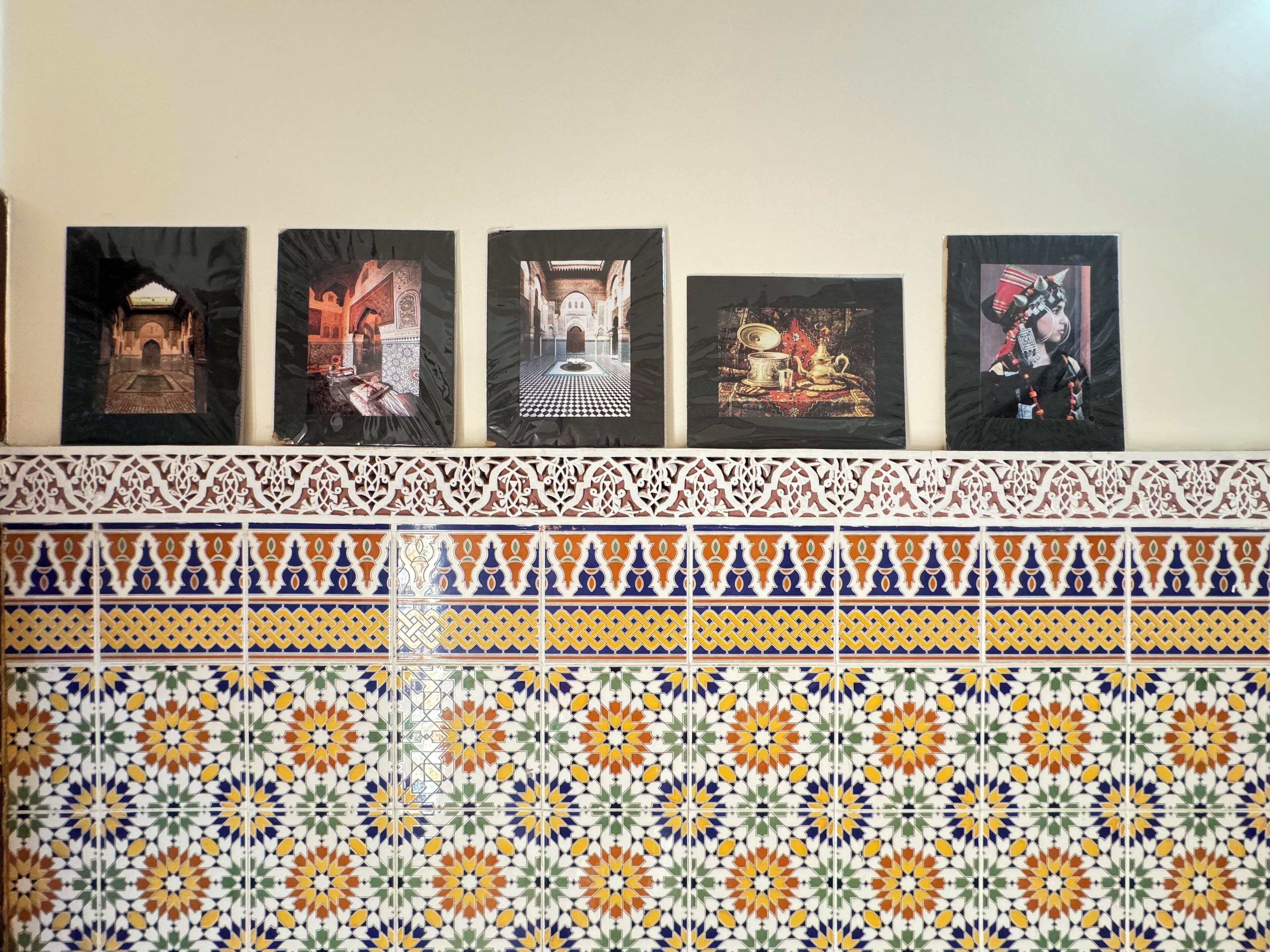Eine Wand mit fünf gerahmten Kunstwerken und einer dekorativen Fliesenleiste.