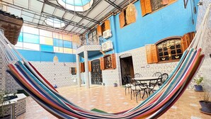 Una hamaca en un patio con suelo de baldosas, una mesa con sillas y una pared azul con detalles decorativos.