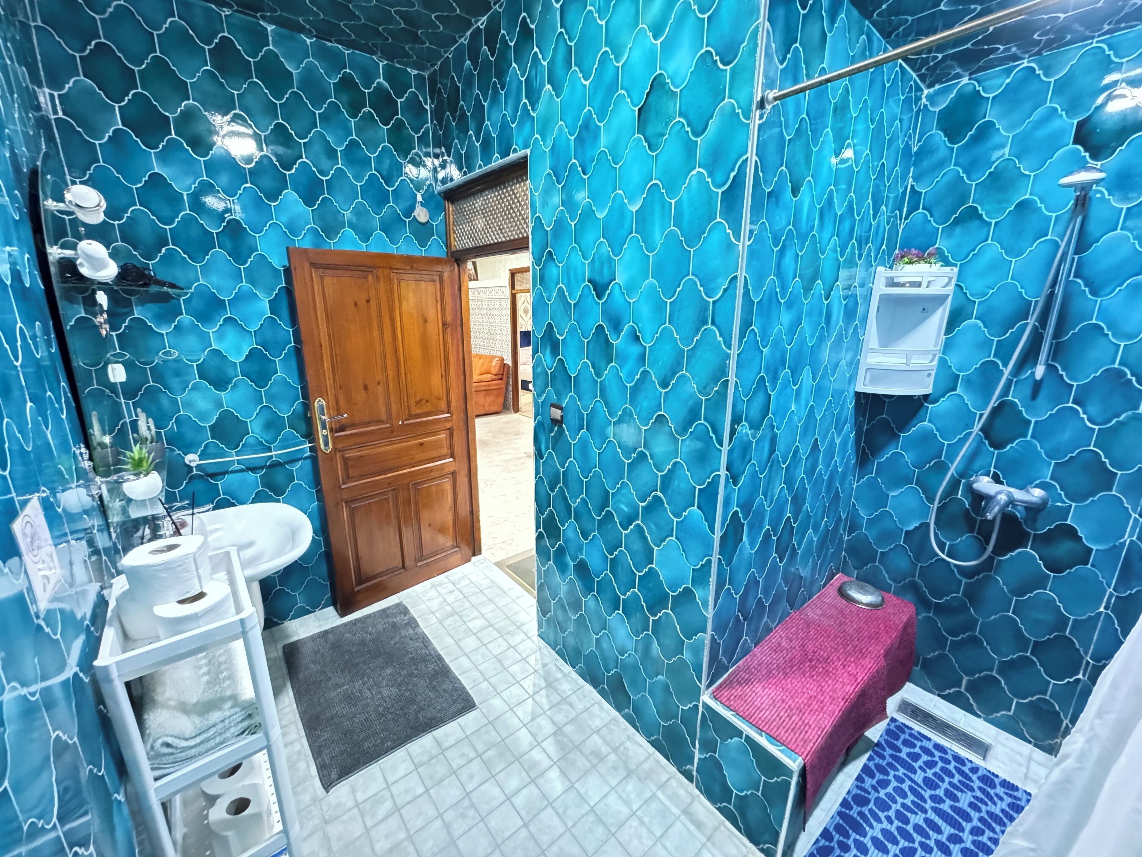 Ein Badezimmer mit blauen Wandverkleidungen, einer Holztür, einem Waschbecken, einer Toilette und einer Duschkabine.