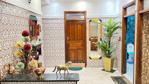 Un pasillo con paredes estampadas, una puerta de madera, un espejo, una planta en maceta y un jarrón decorativo con flores.