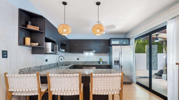 A modern kitchen with a central island, dark cabinetry, and a large window. - Spacious Home w/ Private Pool & Covered Patio Near the Beach (Potrero)