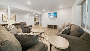 A modern living room with a large sectional sofa, two round coffee tables, and a flat-screen TV mounted on the wall. - Brand new, 3 Bedroom Suite in Fort Morgan! (Fort Morgan)