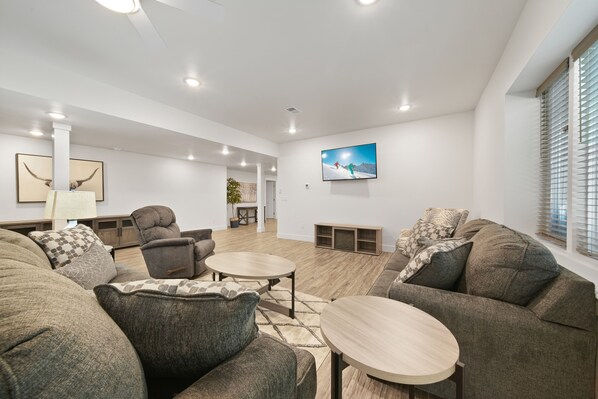 A modern living room with a large sectional sofa, two round coffee tables, and a flat-screen TV mounted on the wall.