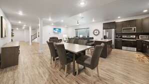 A modern kitchen with dark cabinets, stainless steel appliances, and a wooden dining area with a table and chairs. - Brand new, 3 Bedroom Suite in Fort Morgan! (Fort Morgan)