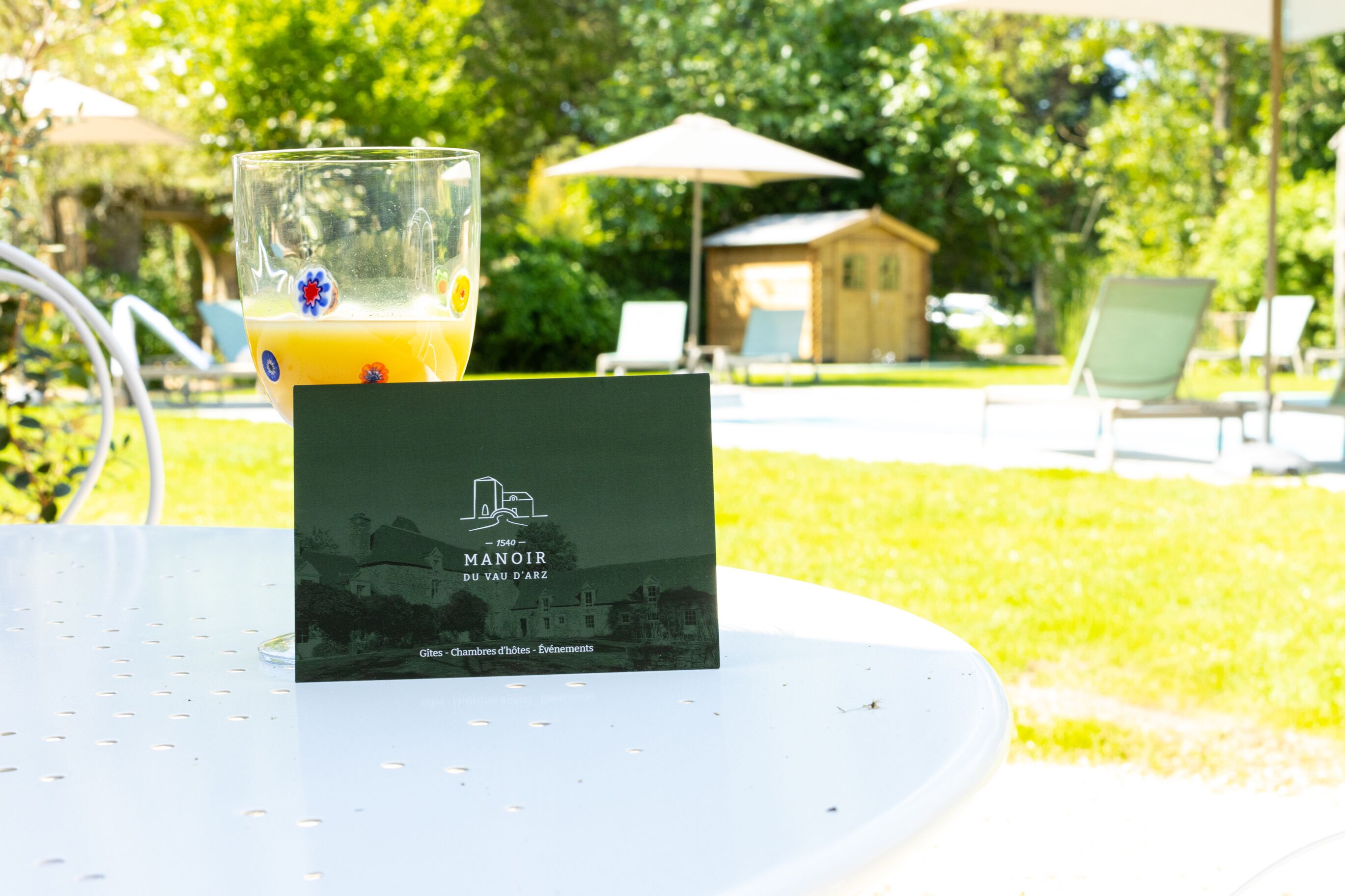 A glass of orange juice on a table with a brochure for Manoir du Vau d'Arcs.