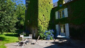 A stone patio with outdoor furniture, a stone wall, and a building partially covered with ivy. - VAU D'ARZ MANOR - Gîte LA GACILLY (MALANSAC)