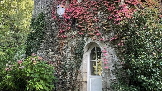 Un bâtiment historique en pierre, avec une façade rouge recouverte de lierre et une petite fenêtre en arc de cercle.