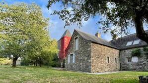Un bâtiment en pierre doté d’un toit en pente, entouré d’une zone herbeuse parsemée d’arbres.