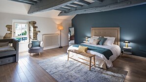 Une chambre avec un grand lit, un banc en bois, un mur en pierre, un radiateur et une fenêtre.