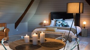 Un dormitorio acogedor con cama, lámparas de noche, una mesita de vidrio con velas y una silla.