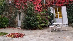 Un edificio con hiedra roja cubriendo sus paredes, un arco de piedra y una zona de estar al aire libre con sillas de metal.