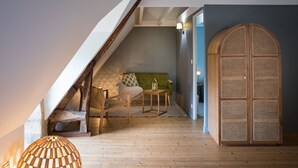 A cozy attic room with a sloped ceiling, a green sofa, a wooden chair, a small table, and a decorative wooden door. - VAU D'ARZ MANOR - Gîte Rochefort (MALANSAC)