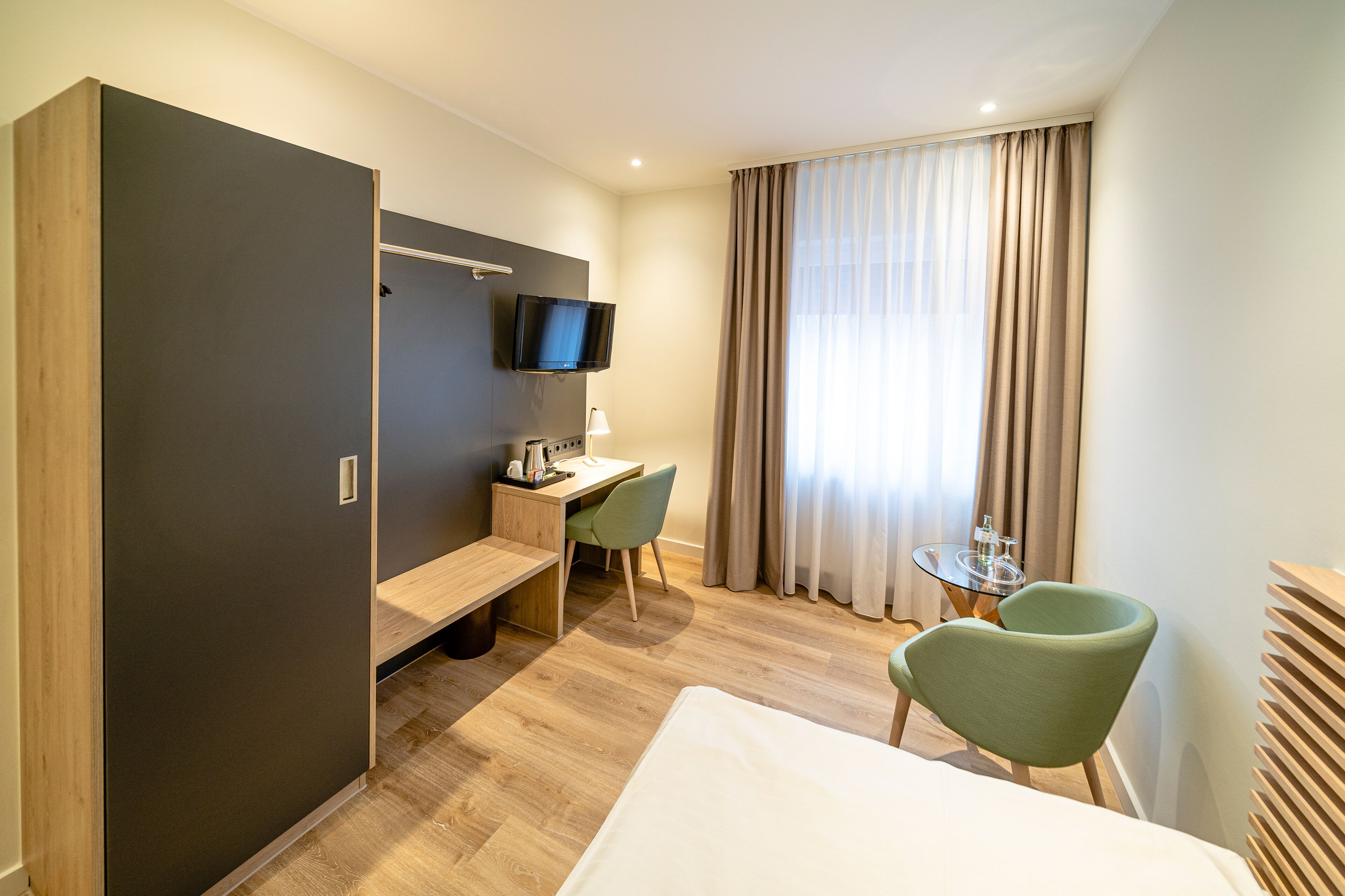 Habitación de hotel con cama, escritorio y silla, televisor en la pared y ventana con cortinas.