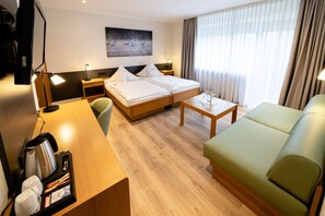 A hotel room with a bed, a desk, a green sofa, a coffee machine, and a painting on the wall. - Hotel Restaurant Kloppendiek  (Vreden)