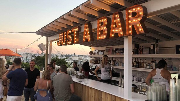 A bar with a sign reading "JUST A BAR" and a view of the city in the background. - 435 East Lake (Montauk)