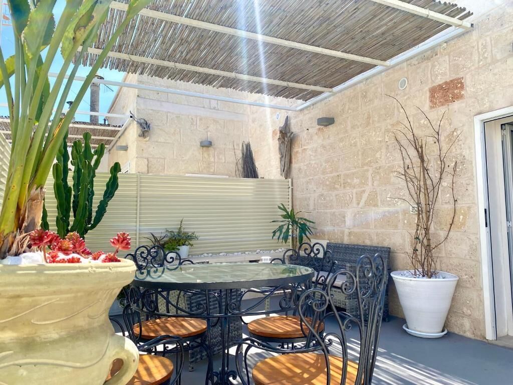 An outdoor patio with a round table and chairs, surrounded by potted plants and cacti.