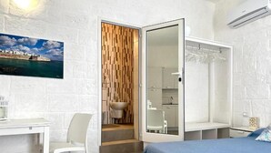 A bedroom with a bed, a desk, a chair, a bathroom with a sink and mirror, and a wooden wall panel.