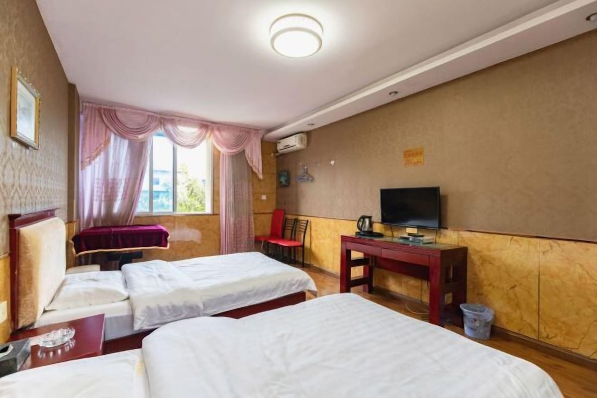 A hotel room with two beds, a desk, a chair, a TV, and a window with curtains.