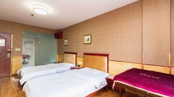 A hotel room with two beds, wooden flooring, a mirror, and a door.